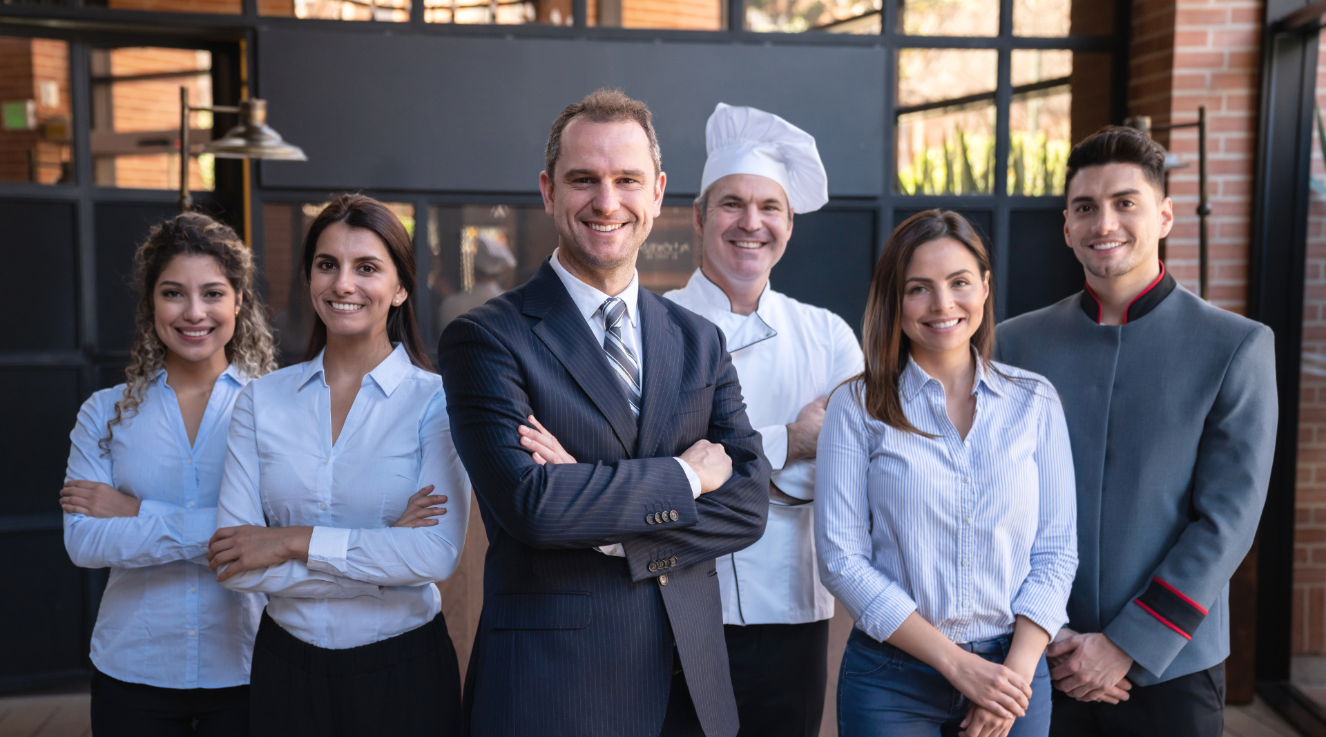 Hotel staff, from all departments, standing at the front of a hotel.